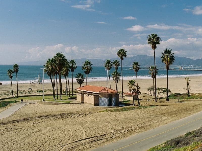 Bike path on a partly cloudy day in Los Angeles by the beach with blue ocean and lots of palm trees: riding a bike on The Strand is one of the best outdoor things to do in Los Angeles!