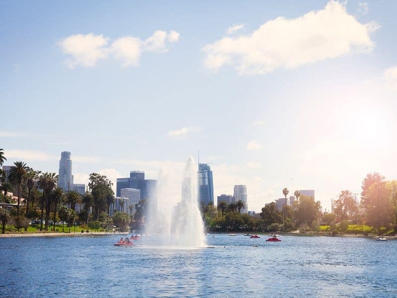 People out enjoying boats on Echo Park Lake in Los Angeles with palm trees and skyscrapers in the background.