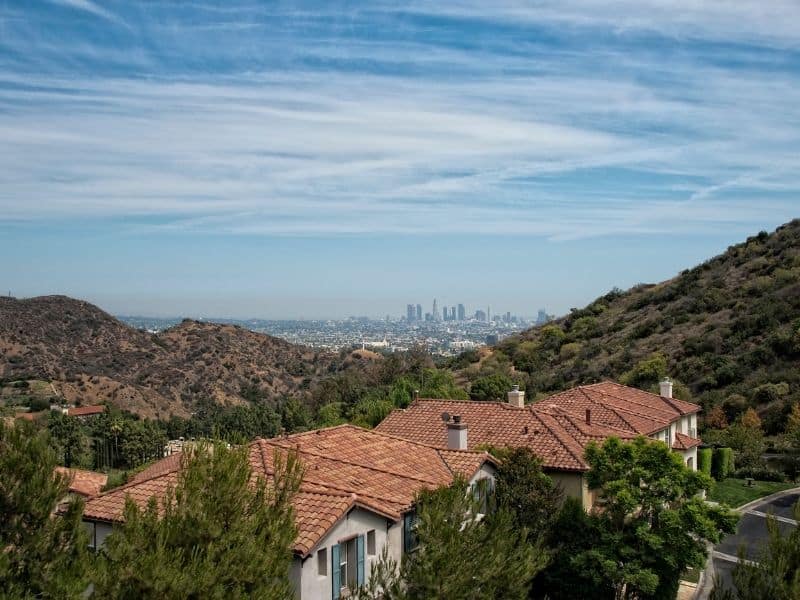 Panorama of Los Angeles as seen from Mulholland Drive: beautiful houses, landscape, and distant cityscape on a sunny day.