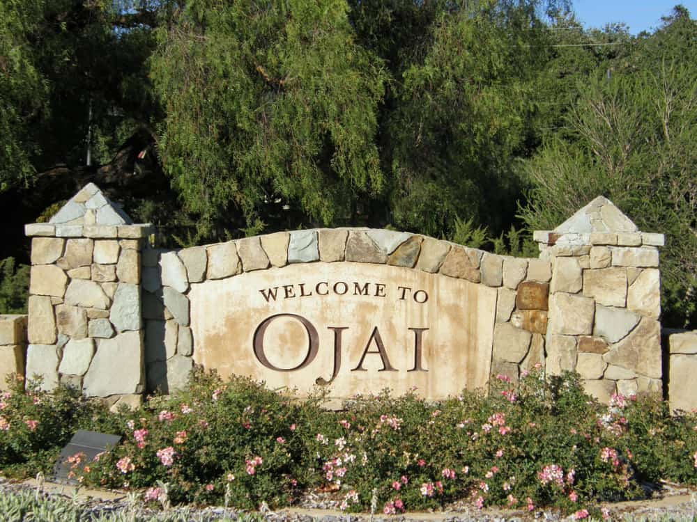 Stone sign which reads "Welcome to Ojai" with flowers and trees behind it.