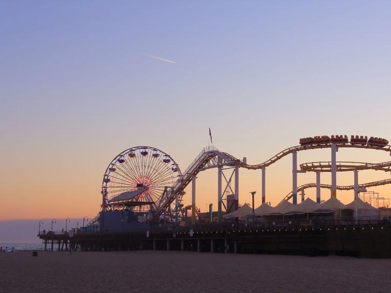 Pastel toned beach sunset in Los Angeles with a view of the roller coaster and Ferris wheel of the Santa Monica pier as well as part of the beach and ocean.