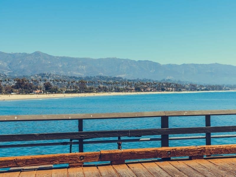 View from the pier of the Santa Barbara wharf, looking onto a clear cerulean beach, with the city in the distance.