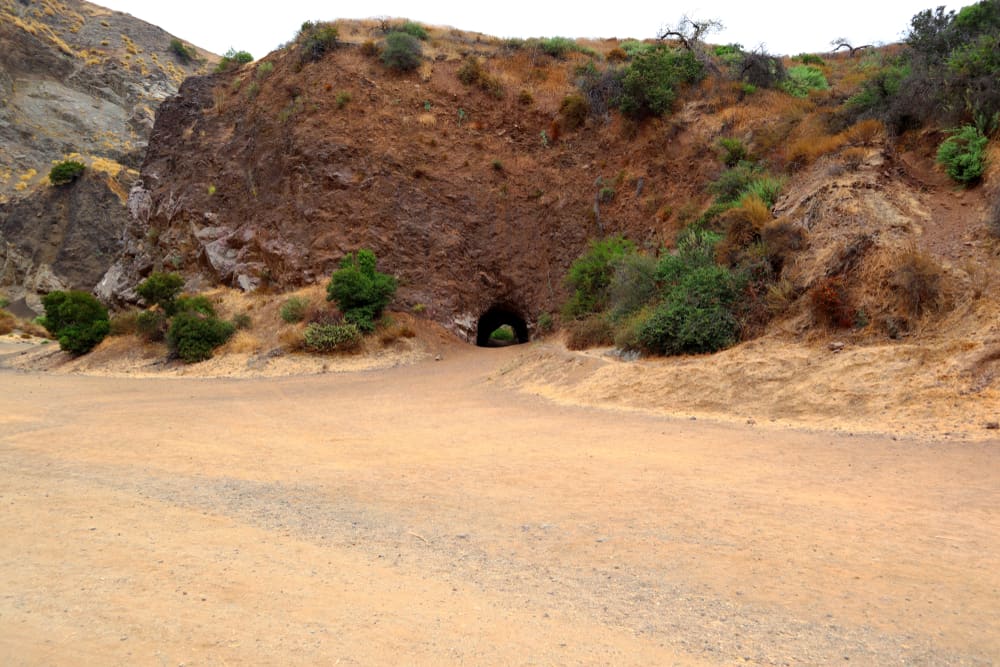 A large road with a small cave located in a reddish-brown rocky hill, seen from the movie "Batman"