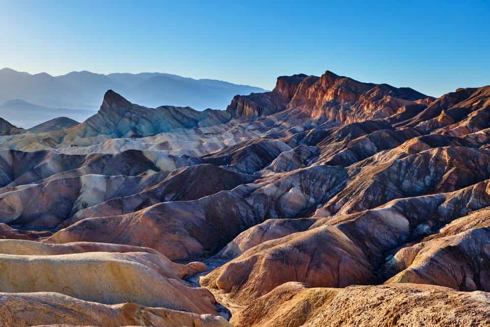 The lunar-looking landscapes of Death Valley National park with red, orange, and purple rippled rocks, on a clear day in the desert.