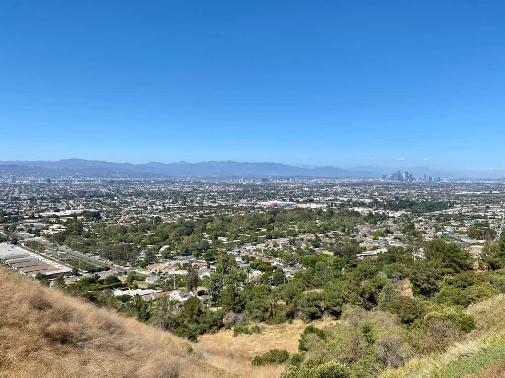 View from up on a hill of a large, sprawling cityscape on a clear blue sky day.