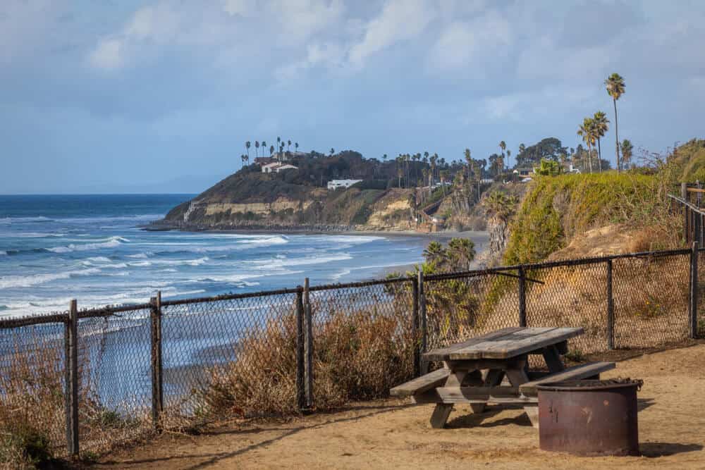 the picnic table at the campsite at san elijo state beach with a view of palm trees, pacific ocean, and swamis cliff