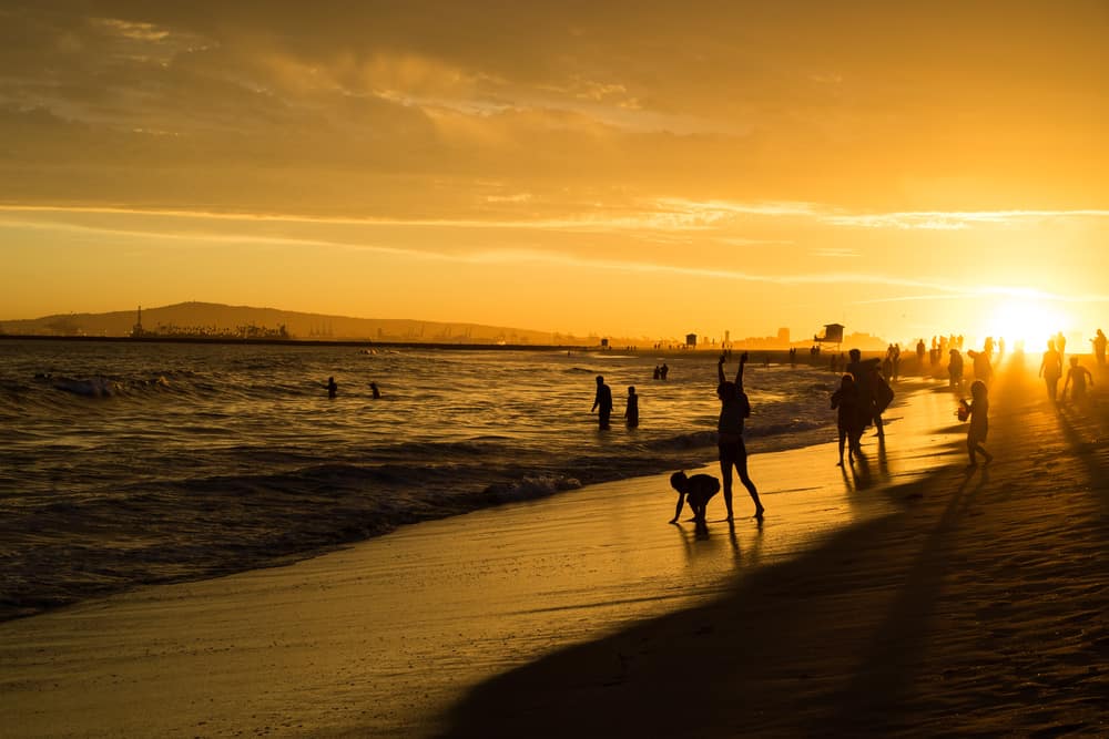 Orange sunset sky with people showing up as black silhouettes playing in the sand and water