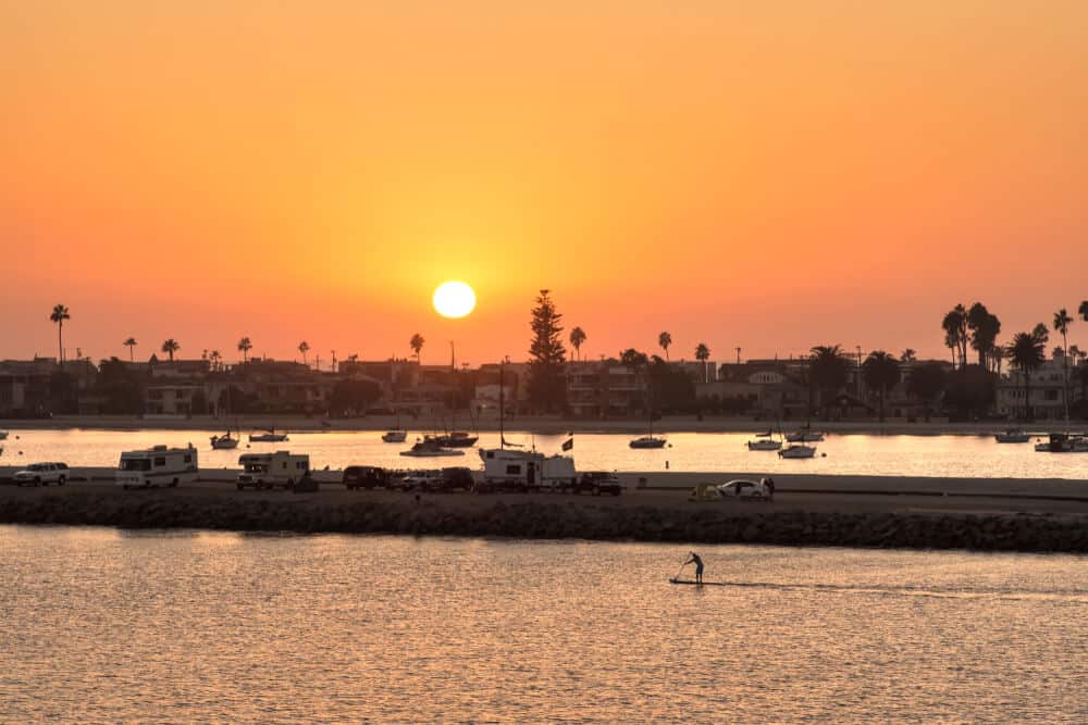 Sunset at the popular San Diego campground "Campland on the Bay", with several RV/campers in front of the water, and one person on a stand up paddle board at sunset