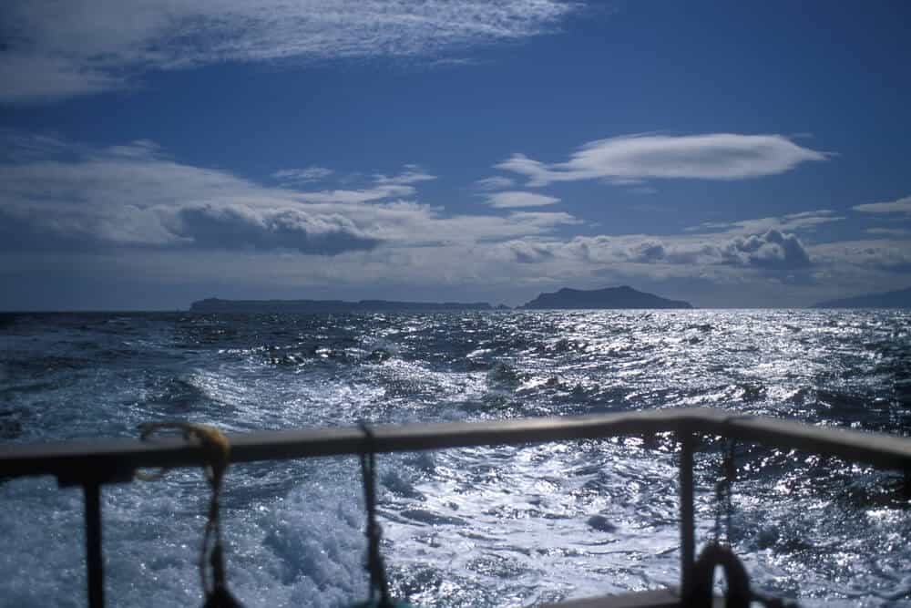 Leaving Channel Islands National Park, looking at the islands receding in the distance from the boat with a metal guardrail in the foreground.