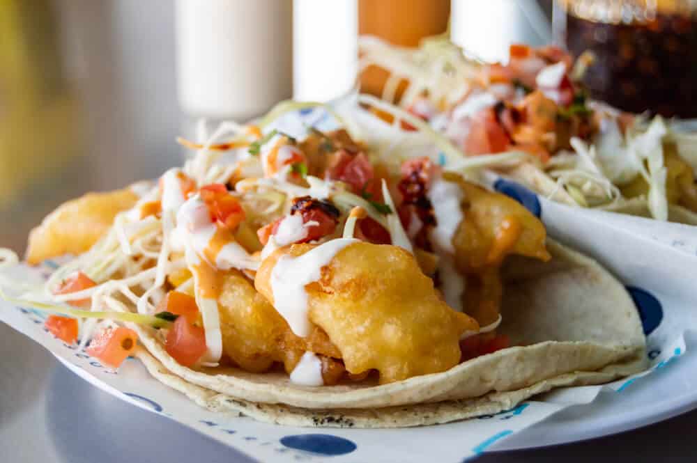 Fish tacos covered in salsa, cabbage, cream, sitting on flour tortillas.