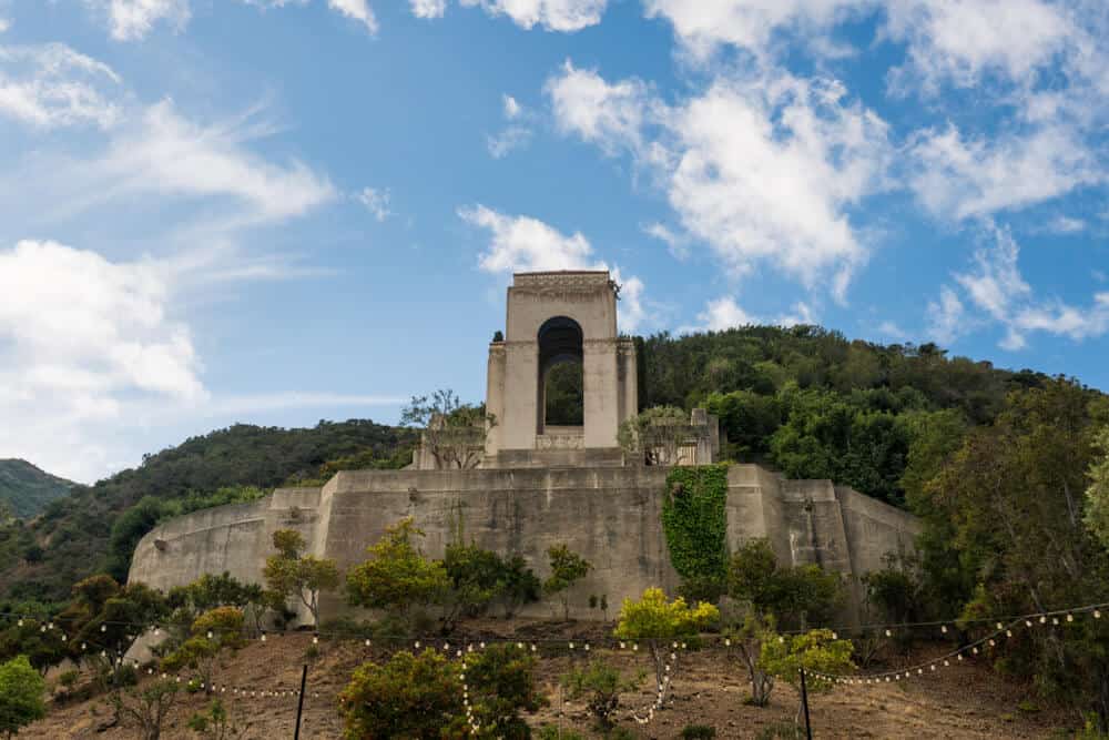 A concrete memorial to Wrigley in a botanic garden with a partly cloudy sky.