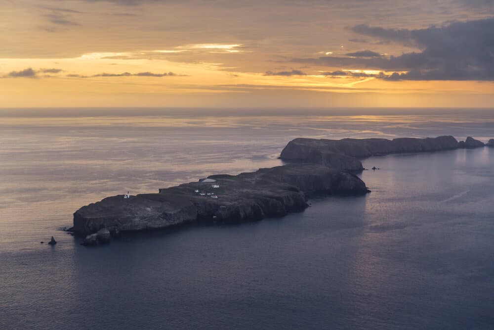 Aerial view over the long and narrow Anacapa Island at sunset, with an orange sky and purplish sea.