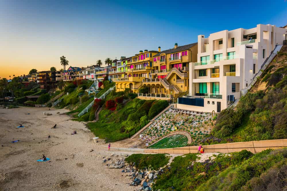 colorful buildings of Corona del Mar in Newport Beach at sunset, with a few people sitting on the beach below the buildings.
