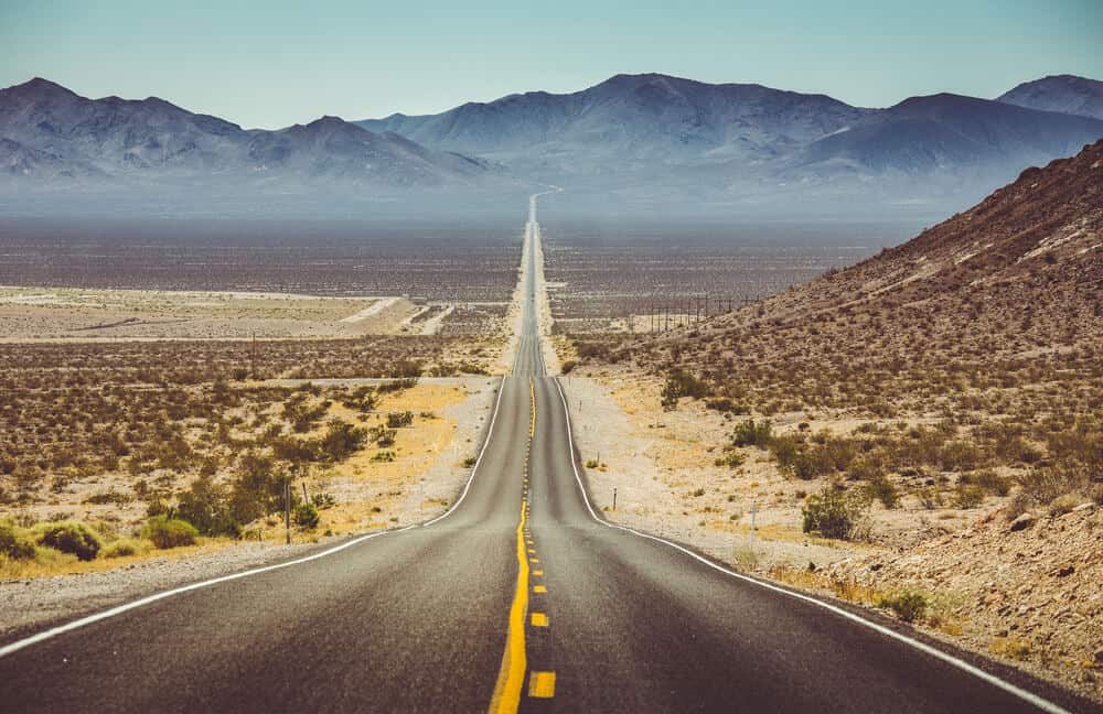 An empty desert road leading to a vanishing pointing the mountains n a sunny day driving towards Death Valley from Los Angeles