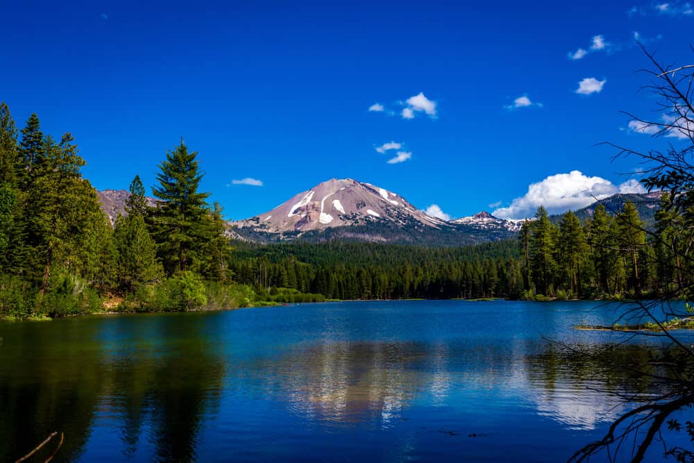 The reflection of a partially snow-covered mountain being reflected in the cerulean blue waters of Manzanita Lake in Lassen Volcanic National Park, a Northern California itinerary must-see!