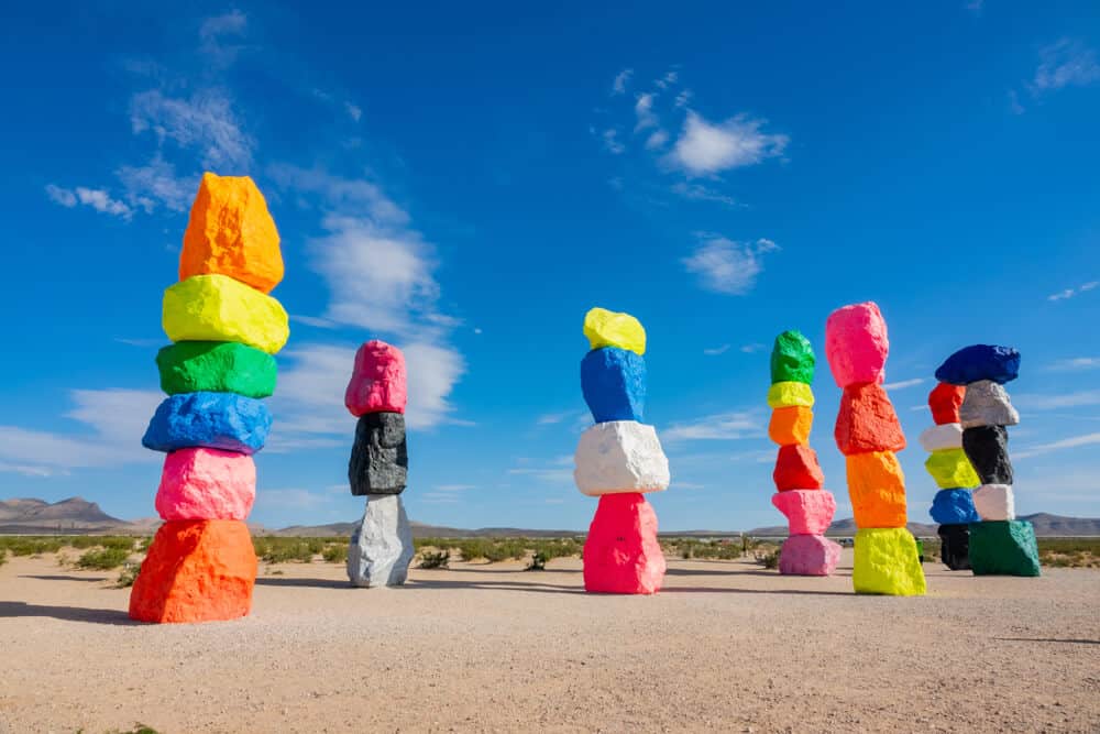 Seven colorful painted stacked rocks in the middle of a desert landscape outside of Las Vegas, a popular road trip stop between LA and Vegas.