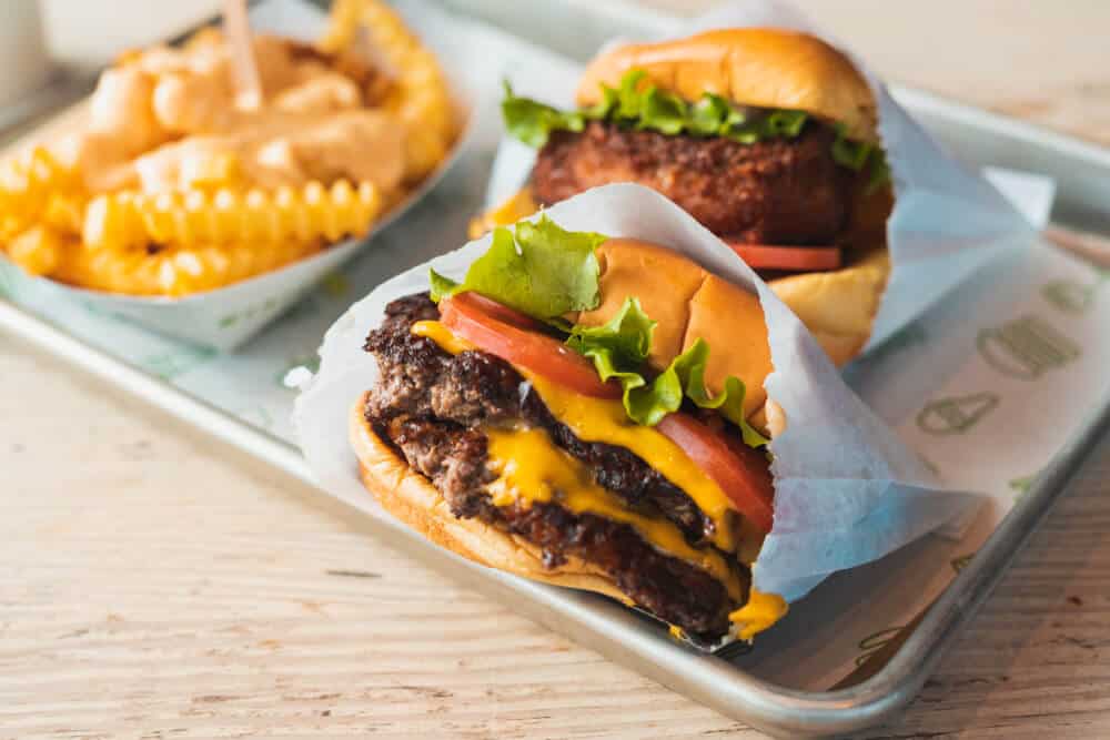 A double cheeseburger and a fried mushroom burger with a side of crinkle cut fries from the burger chain Shake Shack.