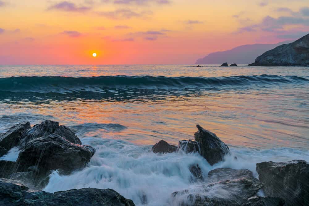 beach on Catalina island at sunset with pink and orange sky and rocks in the water