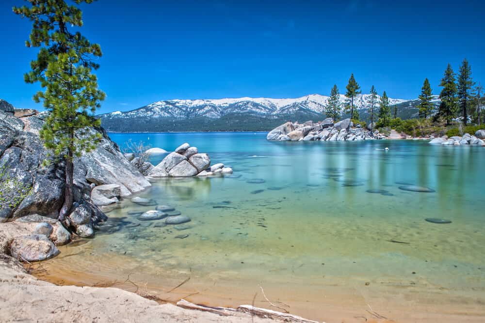 Crystal clear blue and turquoise waters near DL Bliss State Park, part of Lake Tahoe, with mountains covered in snow in the distance.