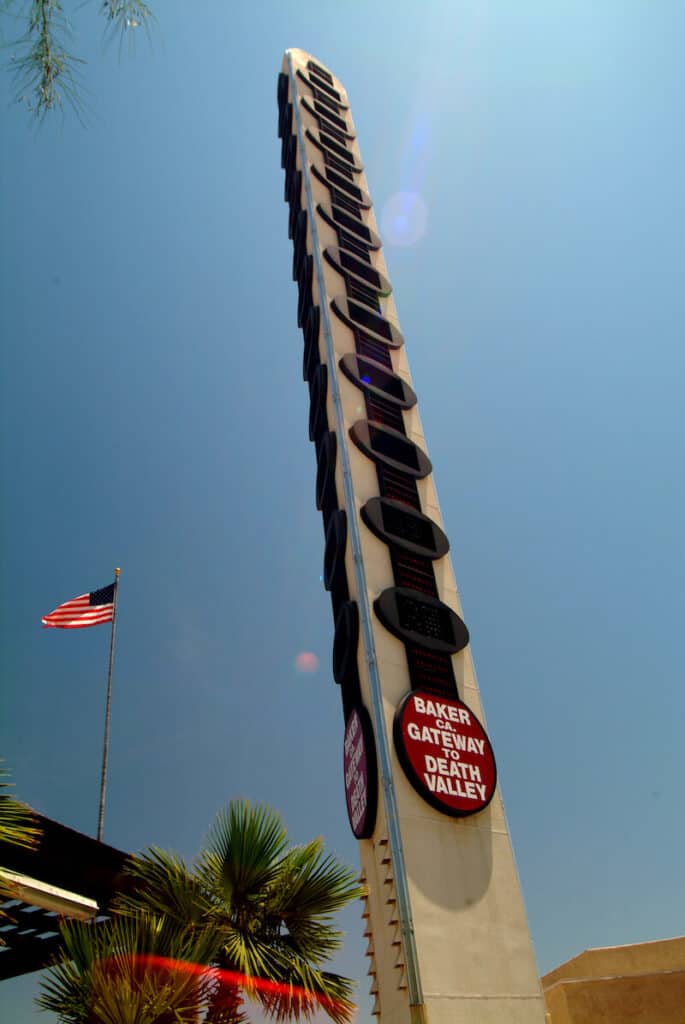 A really tall thermometer which reads "Baker CA Gateway to Death Valley" with an American flag flying in the background.