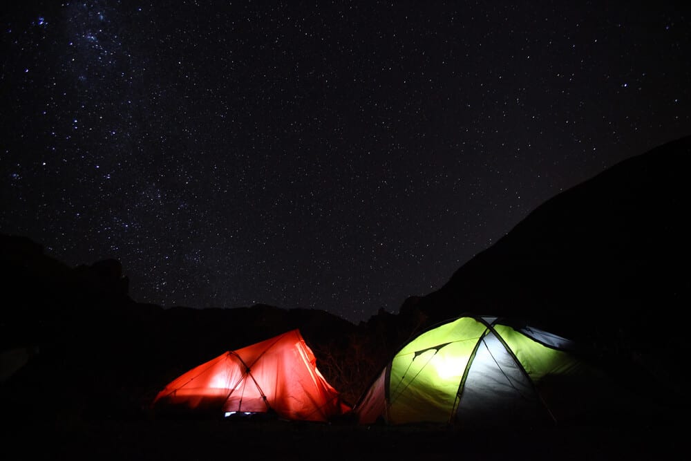 A red and a green tent, both lit up from the inside, against a dark sky sprinkled with lots of tiny little bright stars.