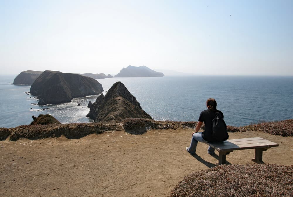 Woman wearing backpack, T-shirt and jeans while sitting on a bench looking at other islands in the Channel Islands chain.