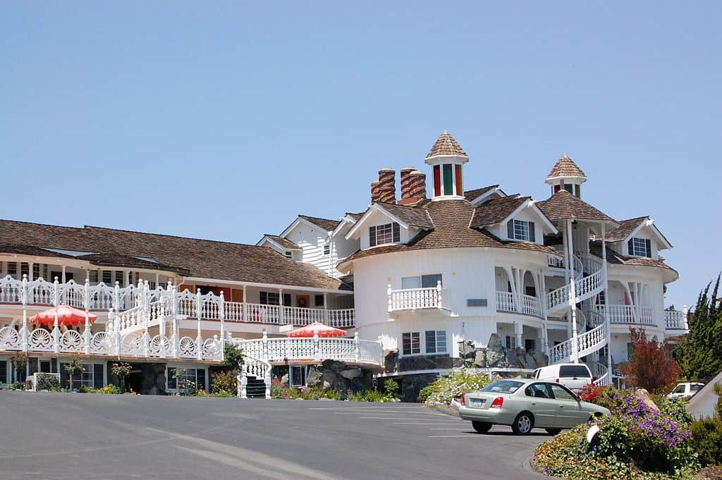 Parking lot in frot of the Madonna Inn, which has unique white railings, rounded architecture, and outdoor spiral staircases to create a quirky looking hotel.