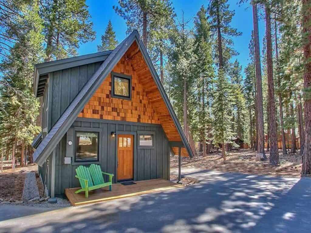 A black and wood patchwork A frame cabin in the woods in tahoe, with a green Adirondack chair in front, a popular Tahoe airbnb choice.