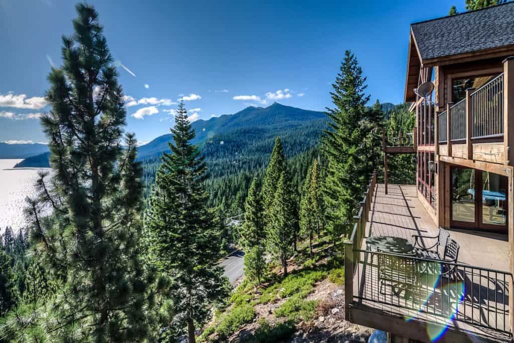 A wide wrap-around deck with gorgeous panoramic views of Lake Tahoe, in front of a cozy modern cabin in Tahoe that sleeps up to 9 guests