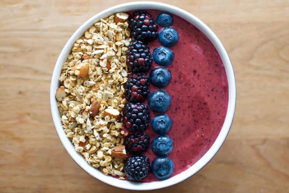 Purplish acai berry smoothie bowl with granola on one side and two stripes of berries: blackberries and blueberries