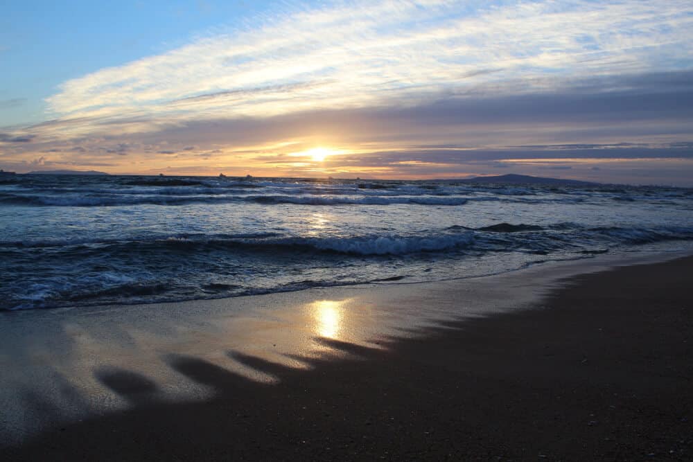 Bolsa Chica State Beach at sunset, with waves crashing in the ocean, sunset mirroring in the water on the dark sand