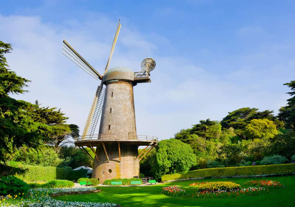 A stone dutch windmill in the middle of a San Francisco park surrounded by greenery and flowers.