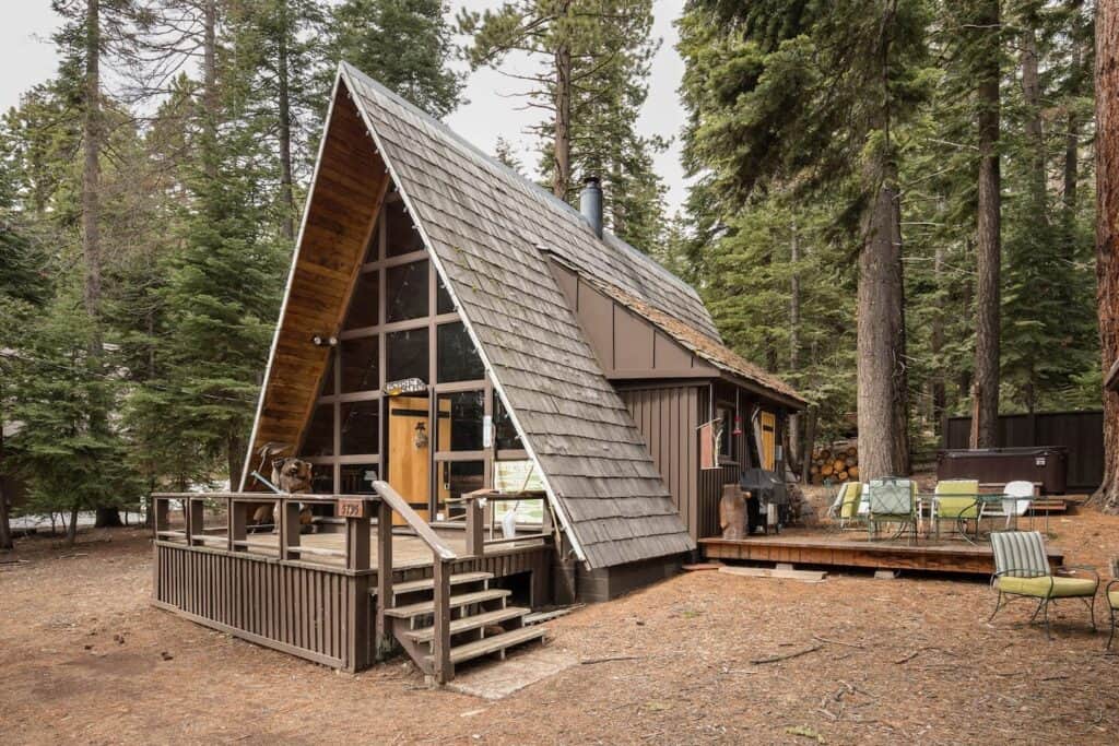 An A-Frame wooden cabin in Tahoe with chairs on an outdoor deck in the forest.