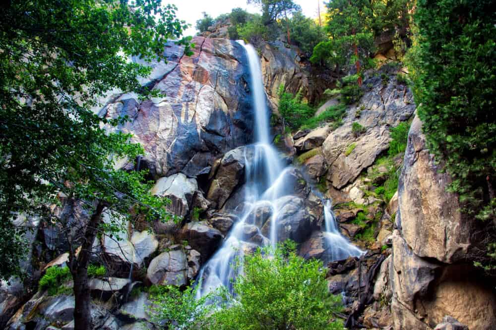 Long exposure waterfall cascading over rocks, surrounded by green trees, on a hike in Kings Canyon National Park