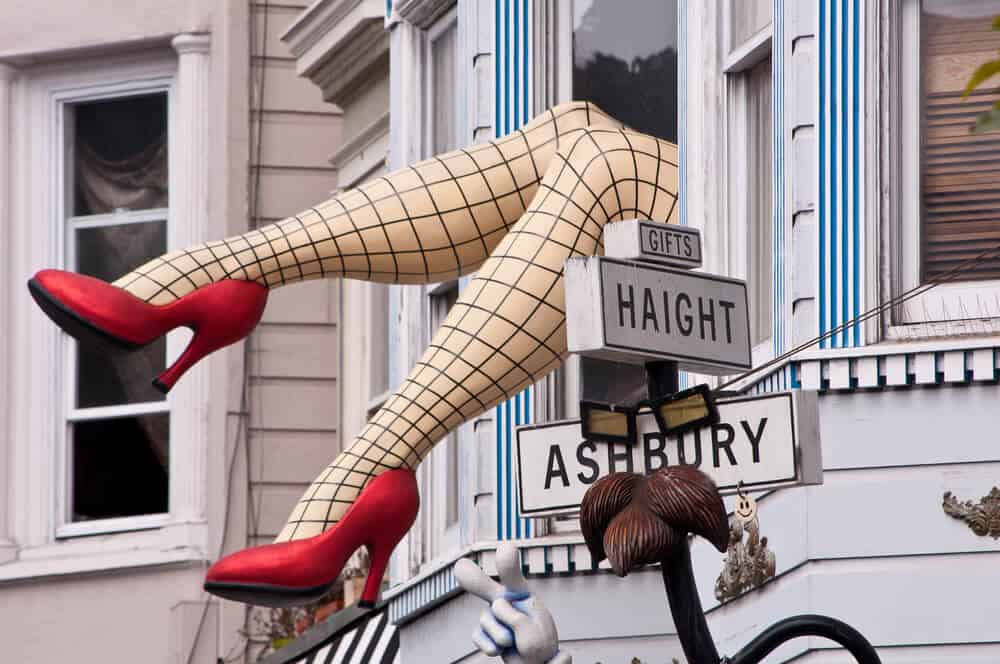 Street signs which say "Haight Ashbury" with a mannequin of model legs wearing fishnets and red high heels coming out of a window