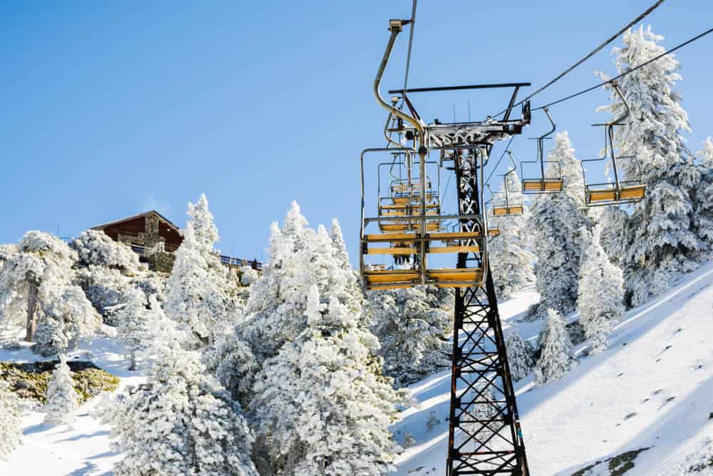 Chair lifts going up on a cable to the top of the Mount Baldy ski resort area, with snow-covered trees on a blue sky day in winter.