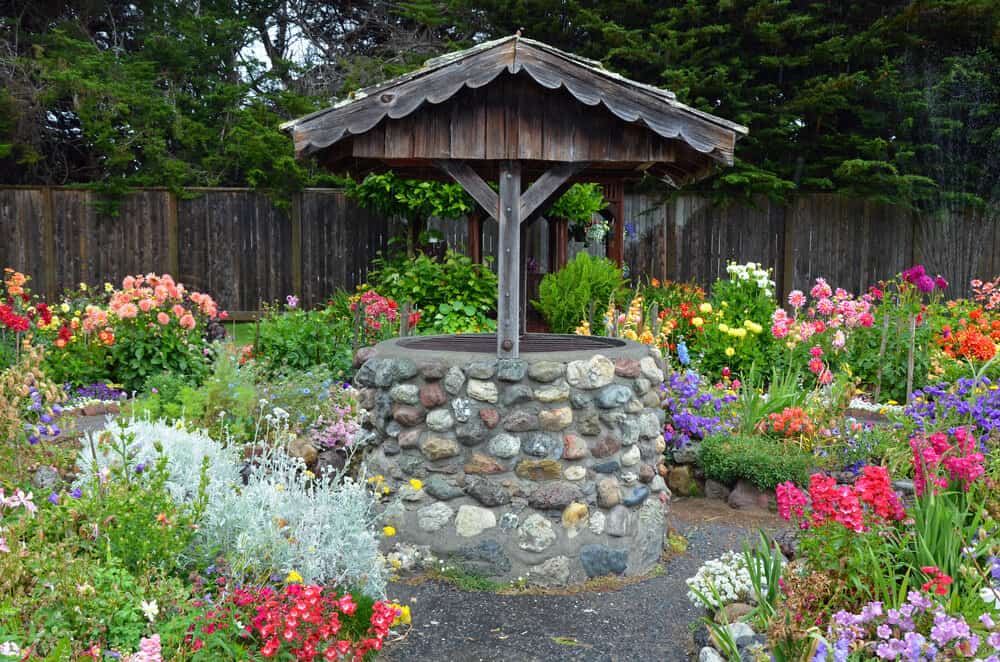 Stone wishing well style well, surrounded by colorful flowers in all shades of the rainbow, in Eureka's Sequoia Park.