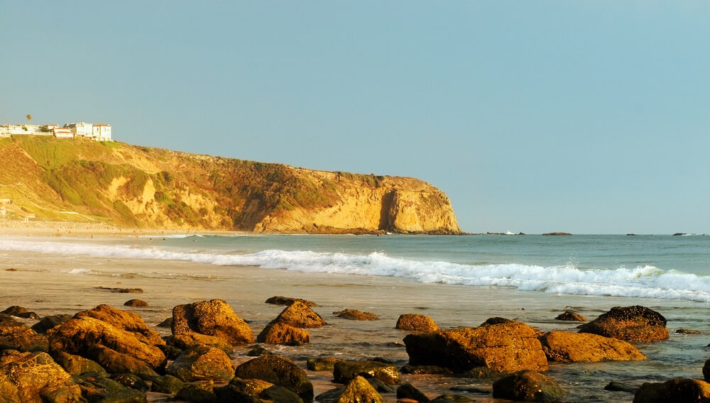 Golden morning light falling on Strand Beach in Dana Point, a popular surf destination for intermediate surfers. Rocks in the foreground.