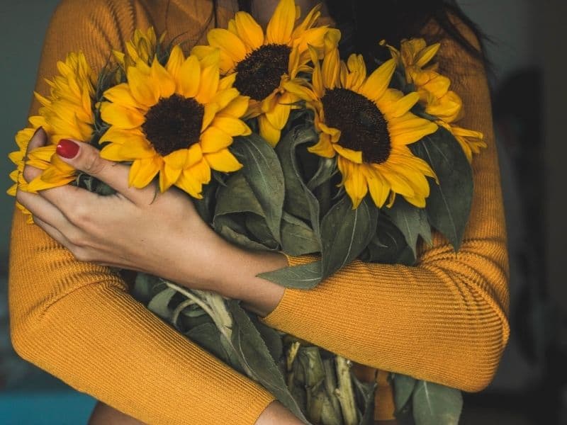 Woman in a yellow long-sleeve shirt holding a bouquet of sunflowers