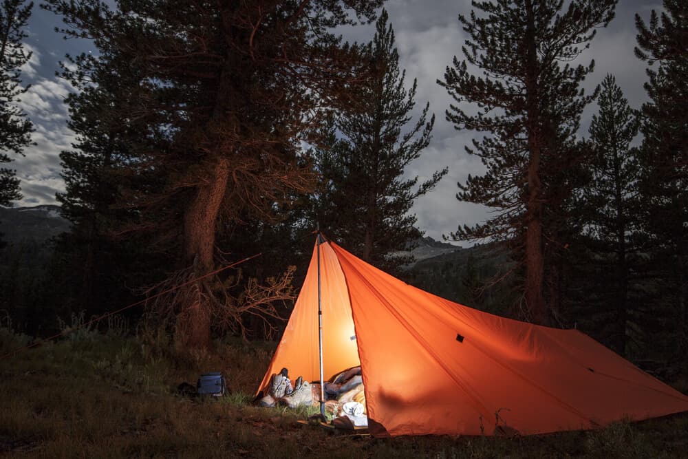 Lit up orange tent in the Yosemite backcountry, with a person inside with a light on. You need a permit for backcountry hiking in Yosemite.