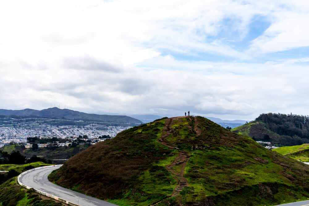 Two small silhouettes at the top of one of the two Twin Peaks, overlooking the city of San Francisco from a popular SF hike