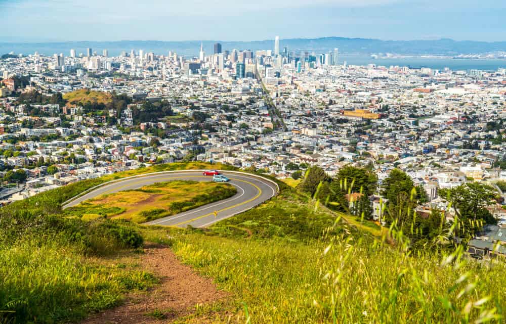 View from Twin Peaks over downtown San Francisco, view of a road with a blue and a red car passing each other on the way up