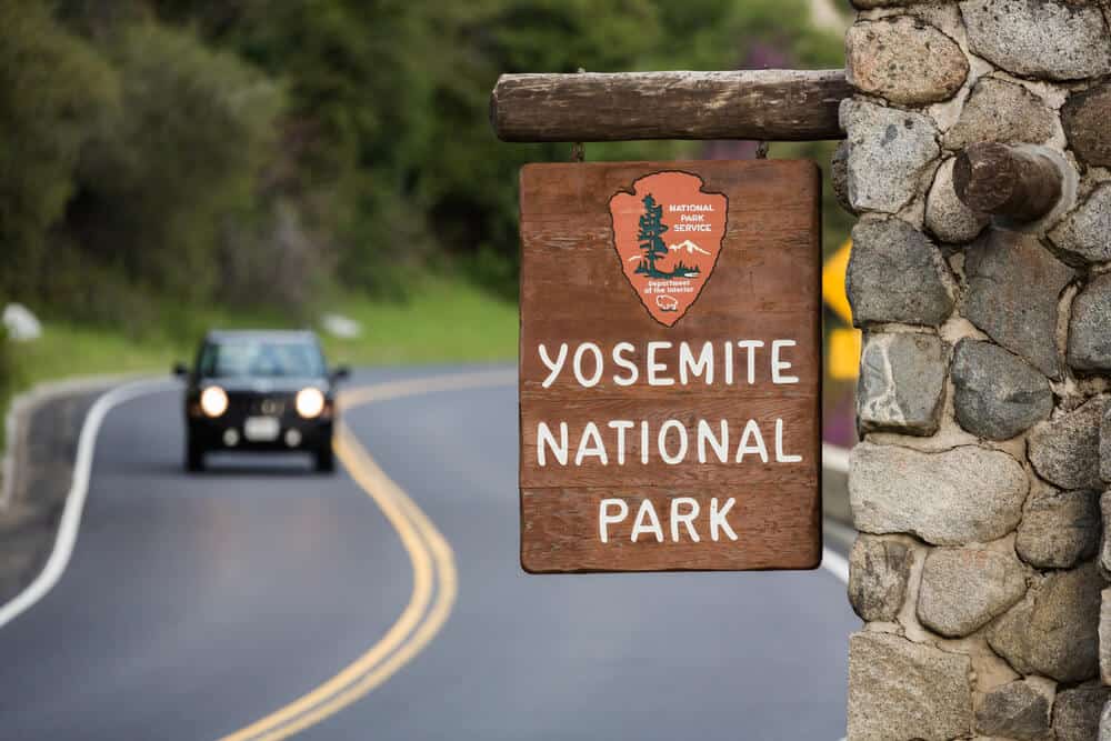 sign for entering Yosemite National Park with a car on the road