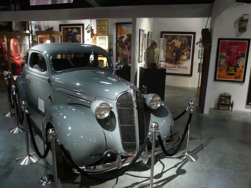 A baby blue vintage car at the Western Museum, surrounded by Western movie posters.