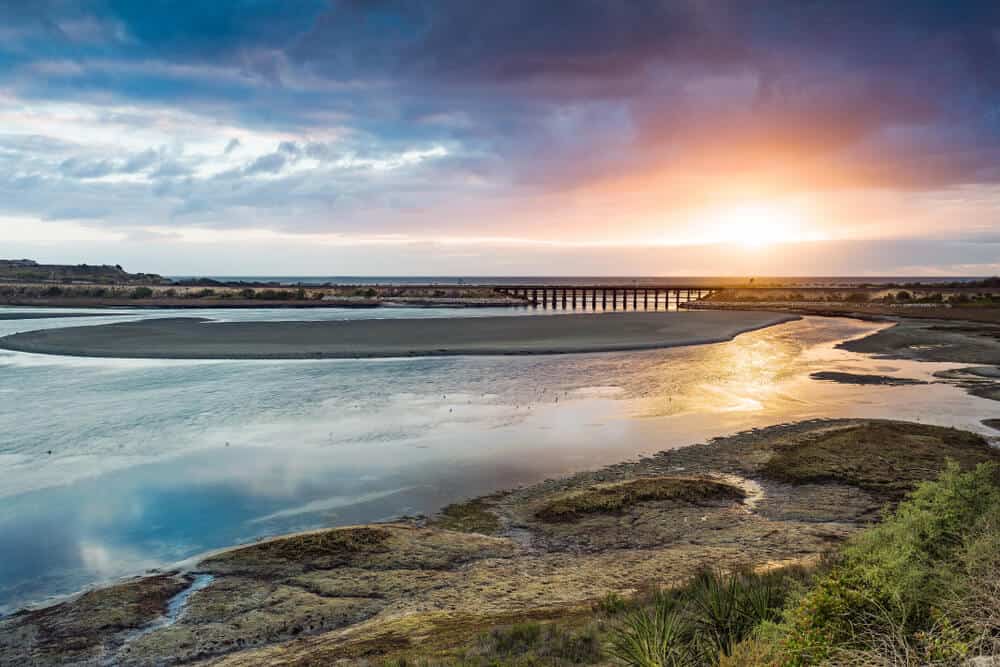 sunset over the pacific ocean near a lagoon with a bridge in the distance