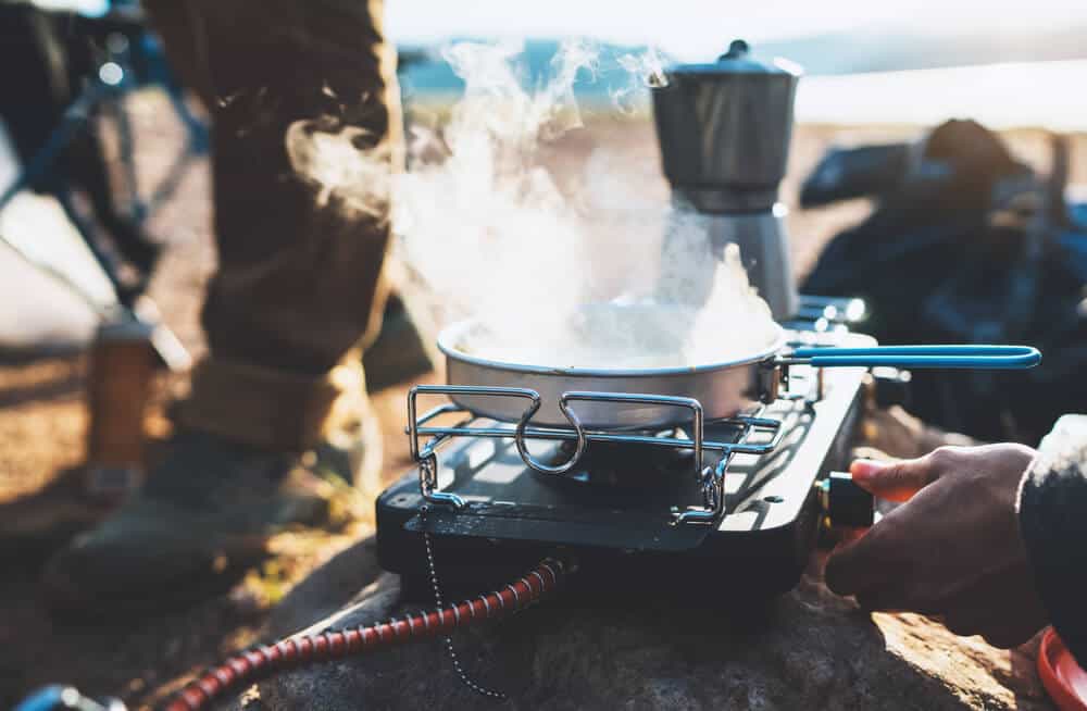 Someone using a camping stove with a Mokapot of coffee also being prepared