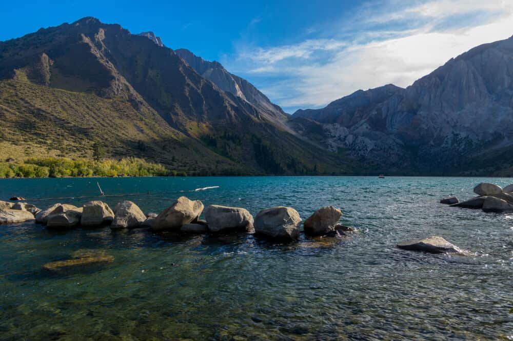 The beautiful turquoise waters of Convict Lake with many boulders in the water with mountains rising above the lake.