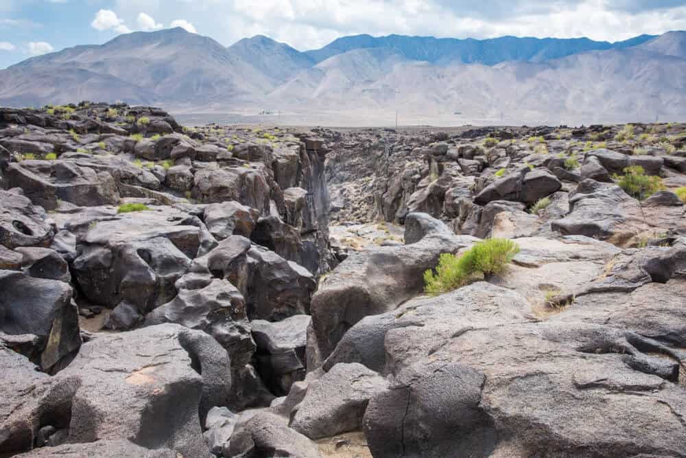 A barren rocky landscape with a small canyon between the rock faces, with high mountains in the background.