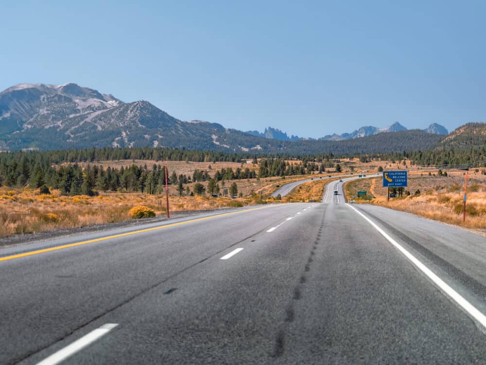 Divided highway, each with two lanes, going through the Eastern Sierra road tripping in California. Blue sky and trees surrounding.