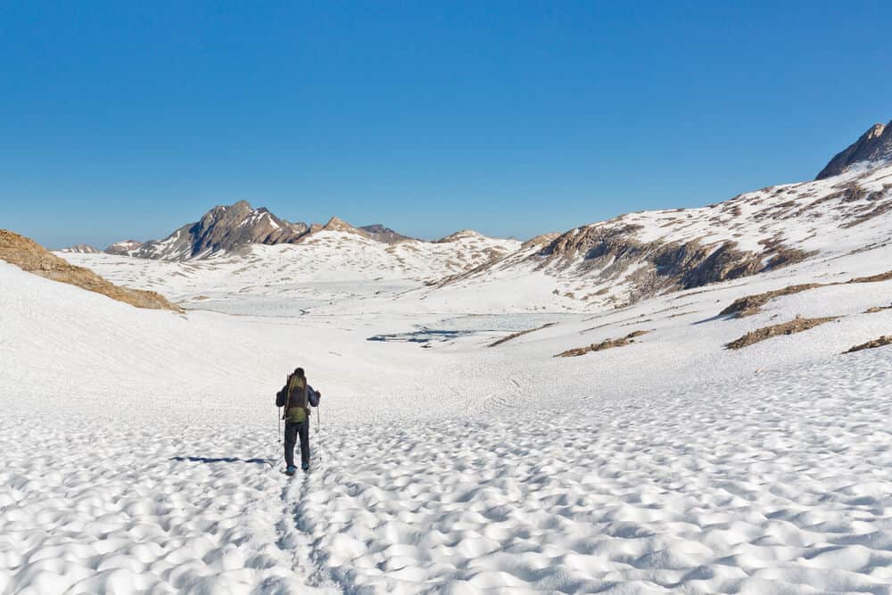 Hiker with trekking poles hiking through the snowpack in Sierras